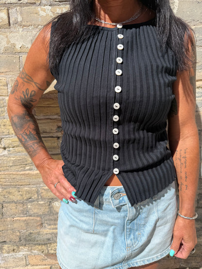 Person wearing a black pleated top with white buttons and light blue denim shorts on a wooden floor.