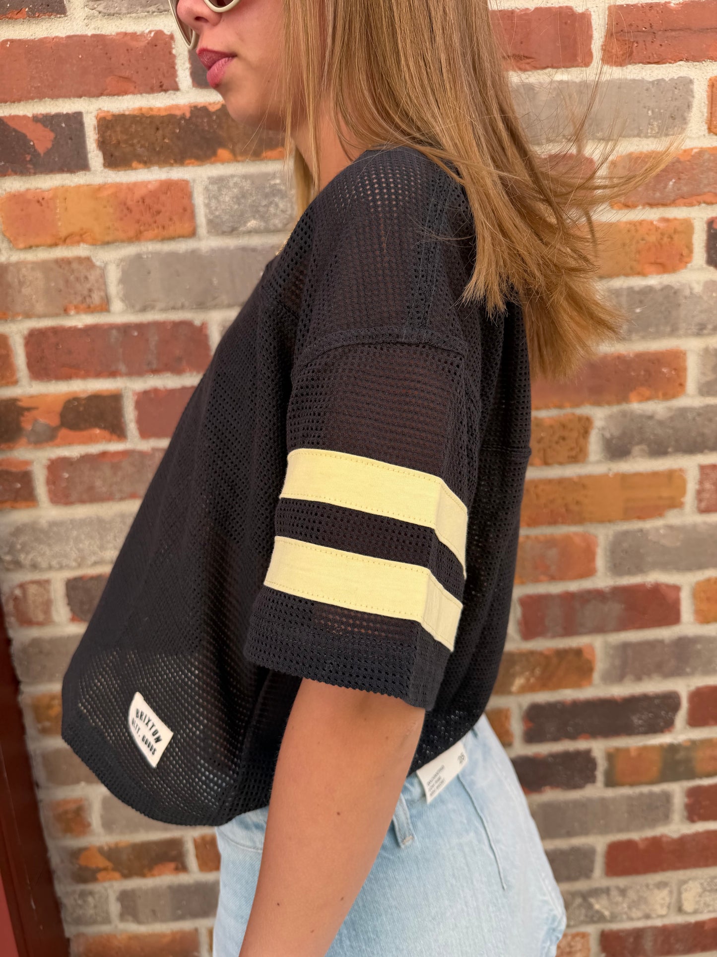 Person wearing a black cap with yellow stripes against a brick wall.