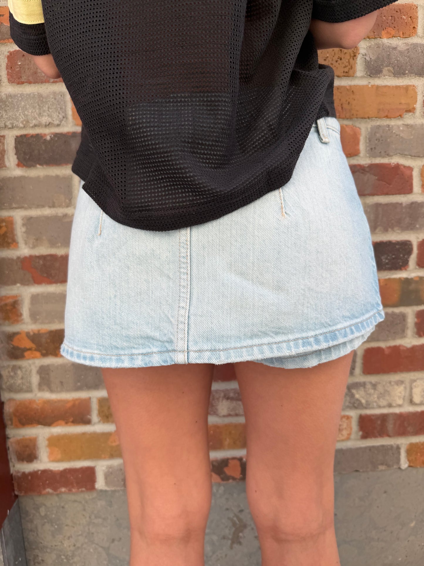 Close-up of a person wearing rolled-up light blue jeans and black shoes on a brick pavement.