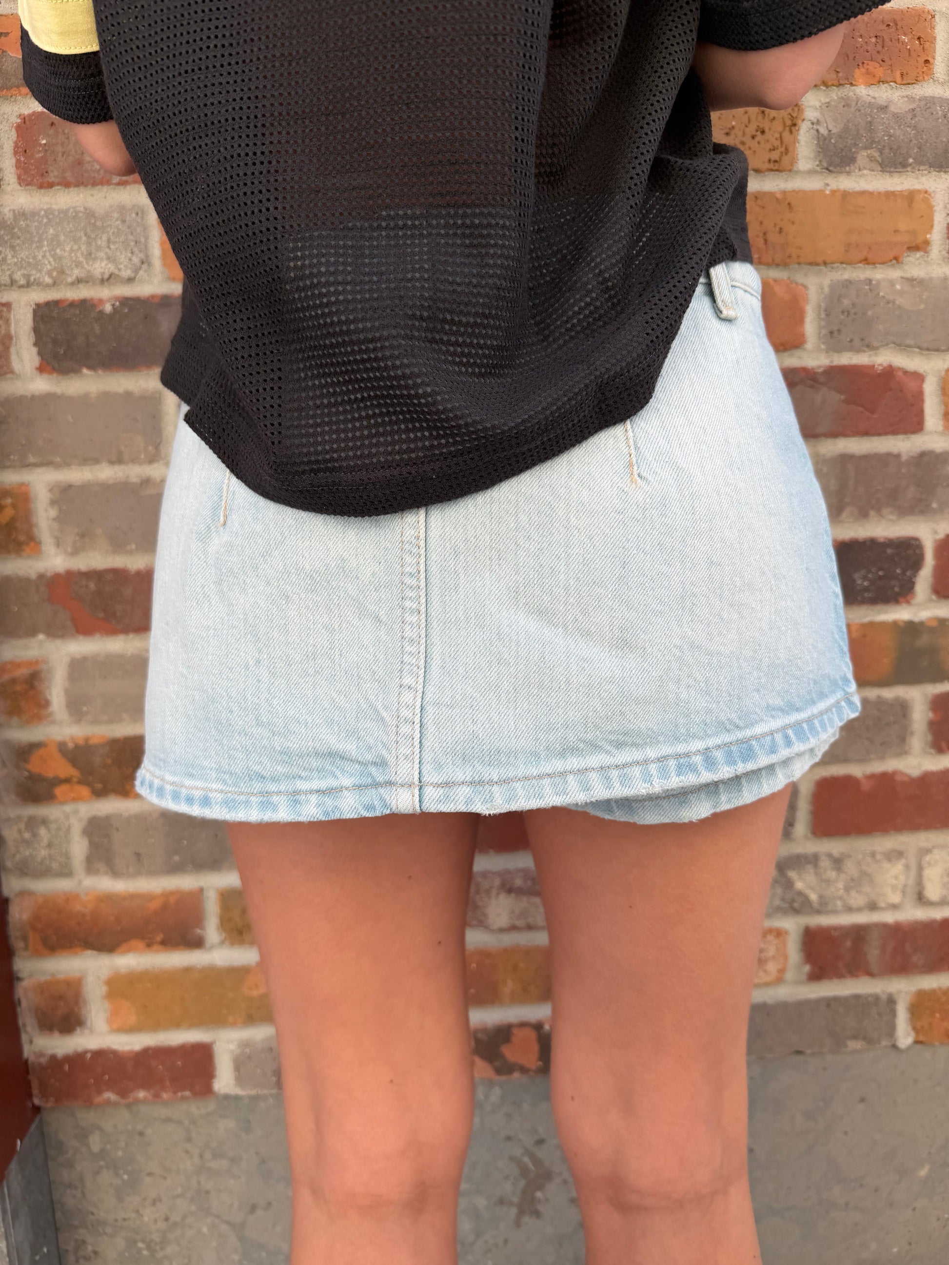 Close-up of a person wearing rolled-up light blue jeans and black shoes on a brick pavement.