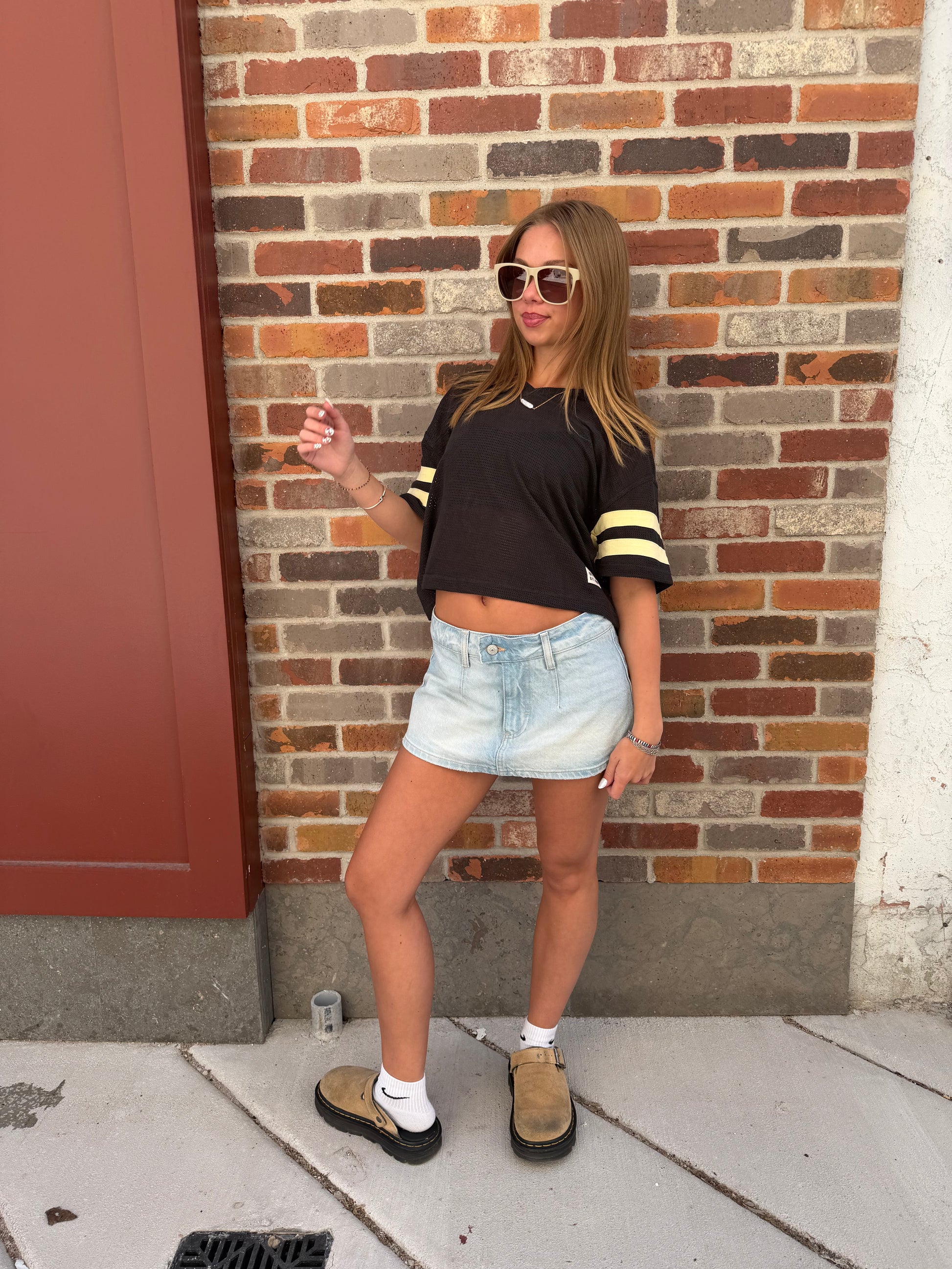 Person standing on a sidewalk with a brick wall background