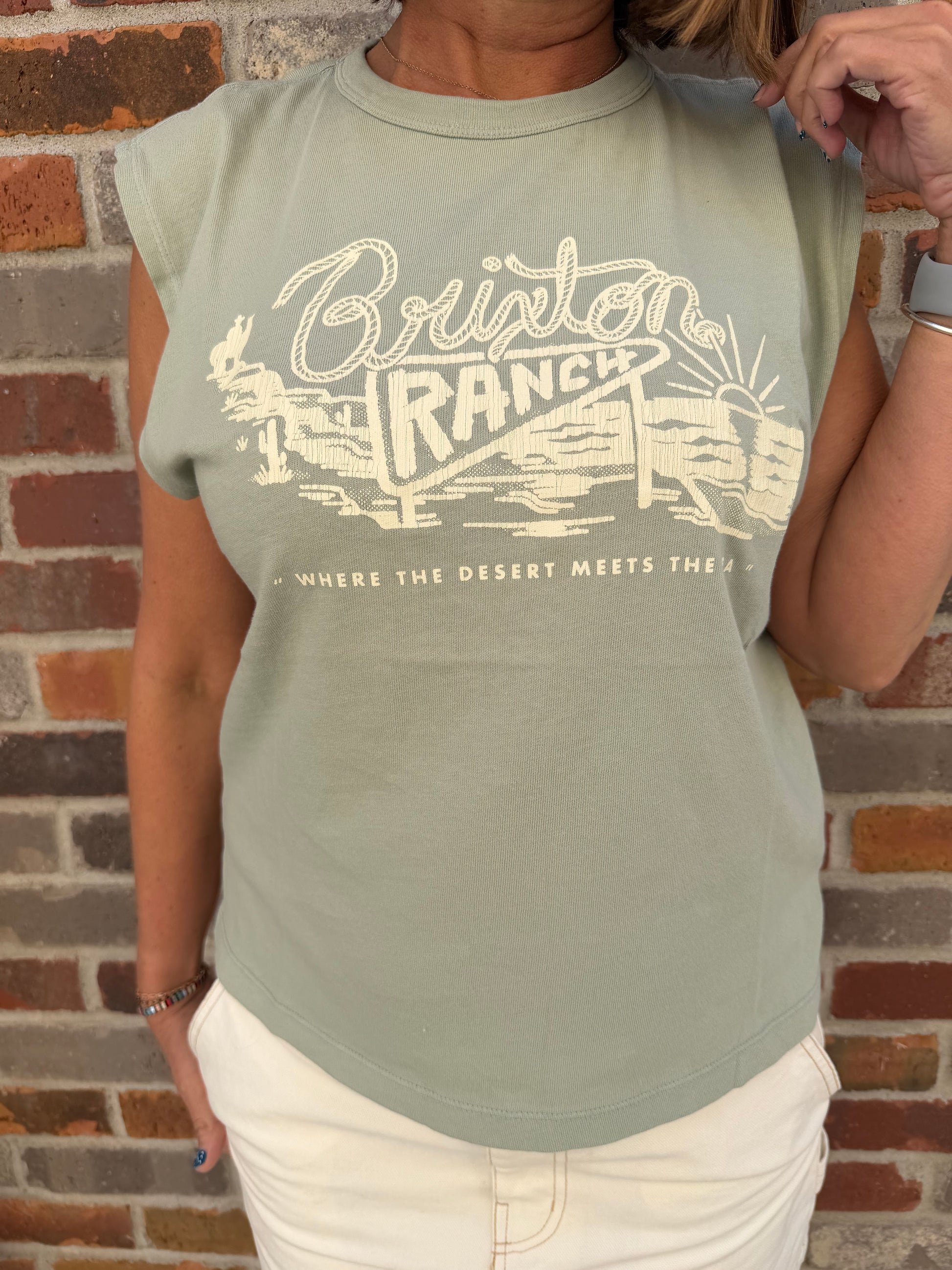 Person wearing a light green t-shirt with a graphic design in front of a brick wall.