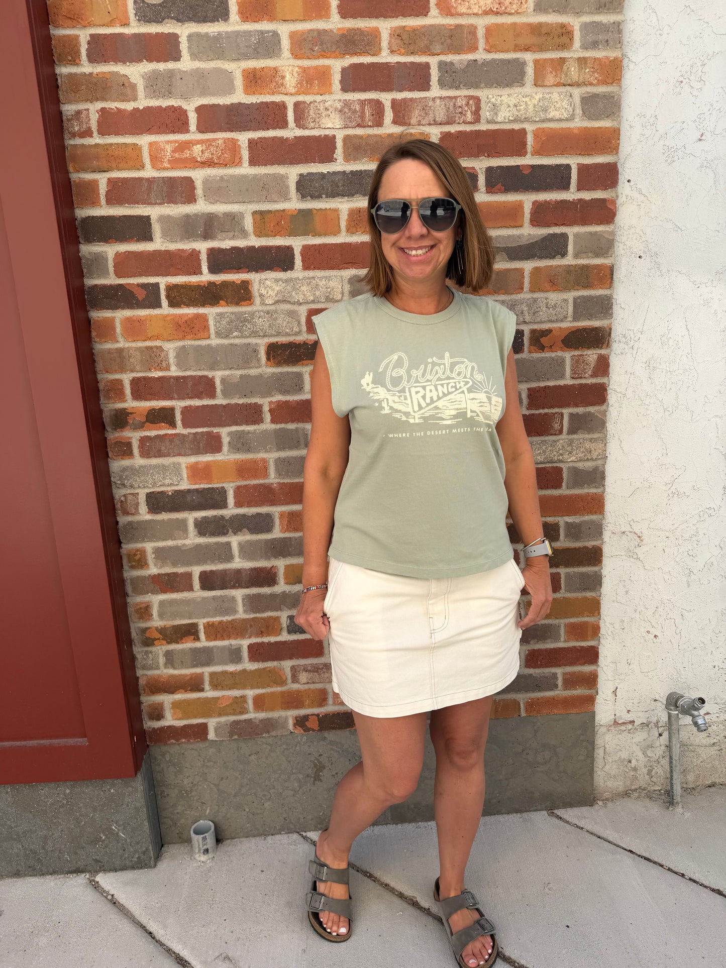 Woman standing on a brick pavement wearing sunglasses and a green shirt.