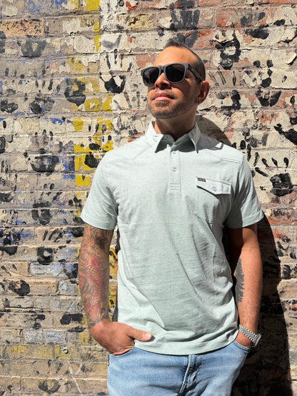 Man wearing sunglasses and a light shirt standing on a textured floor.