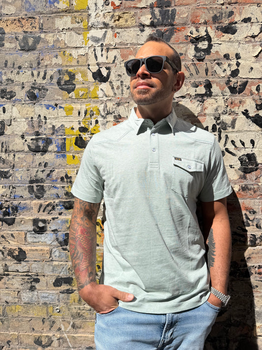 Man wearing sunglasses and a light shirt standing on a textured floor.