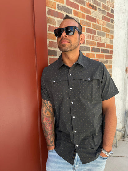 Man wearing a black patterned shirt with white buttons on a red and brown brick pavement.