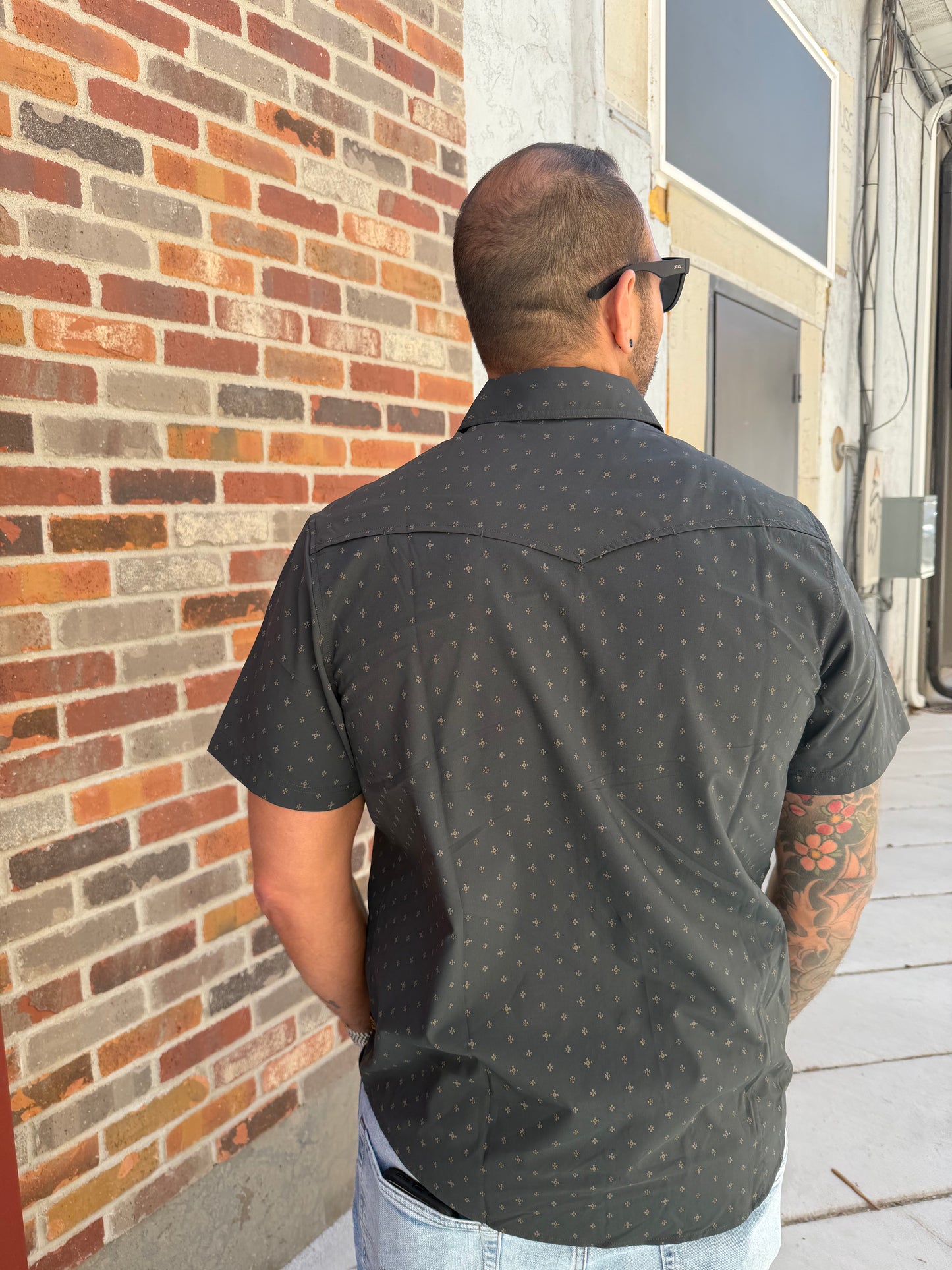 Person wearing a dark shirt with small patterns on a brick pavement.
