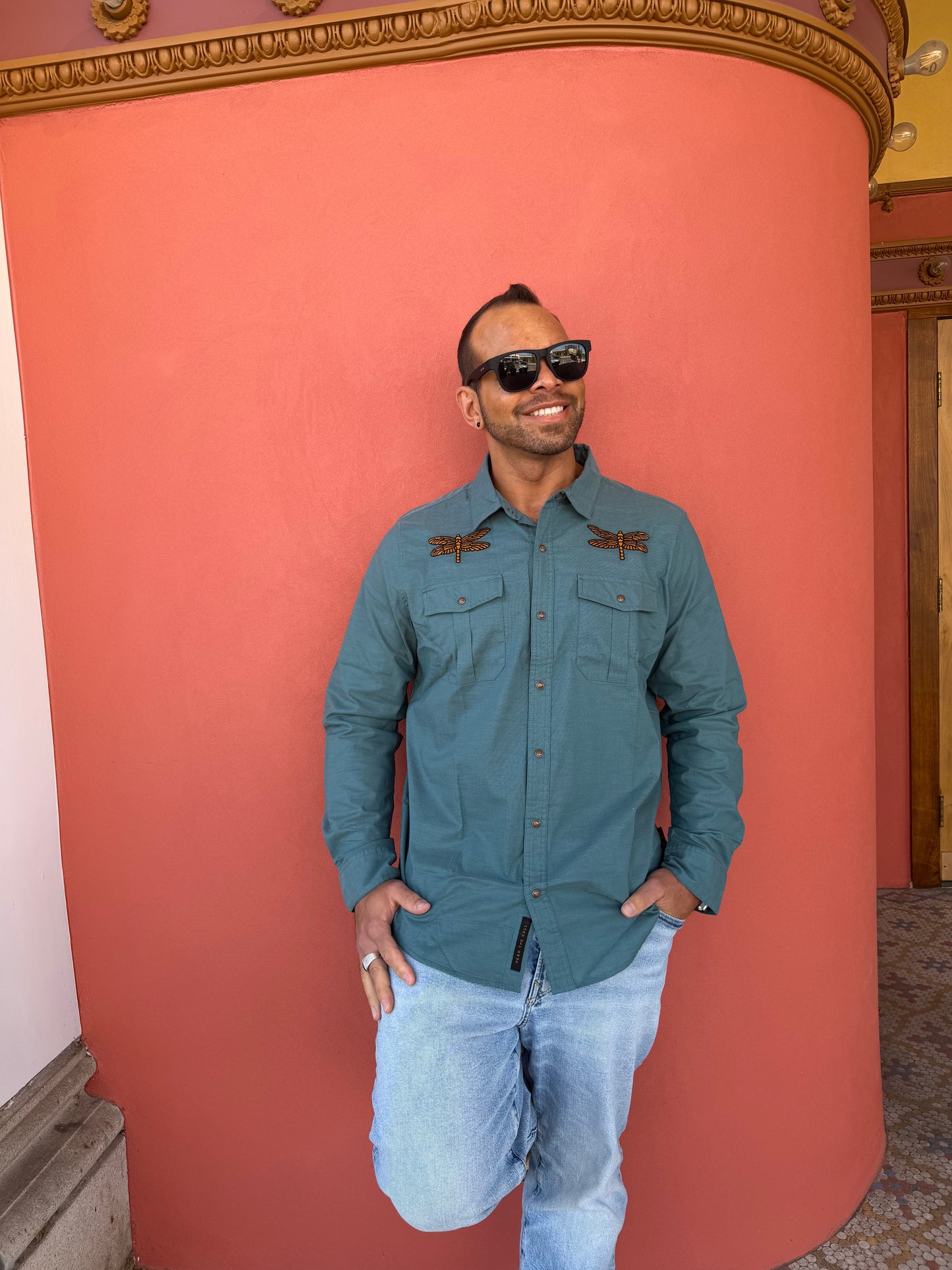 Person wearing a teal jacket and sunglasses on a pink wall