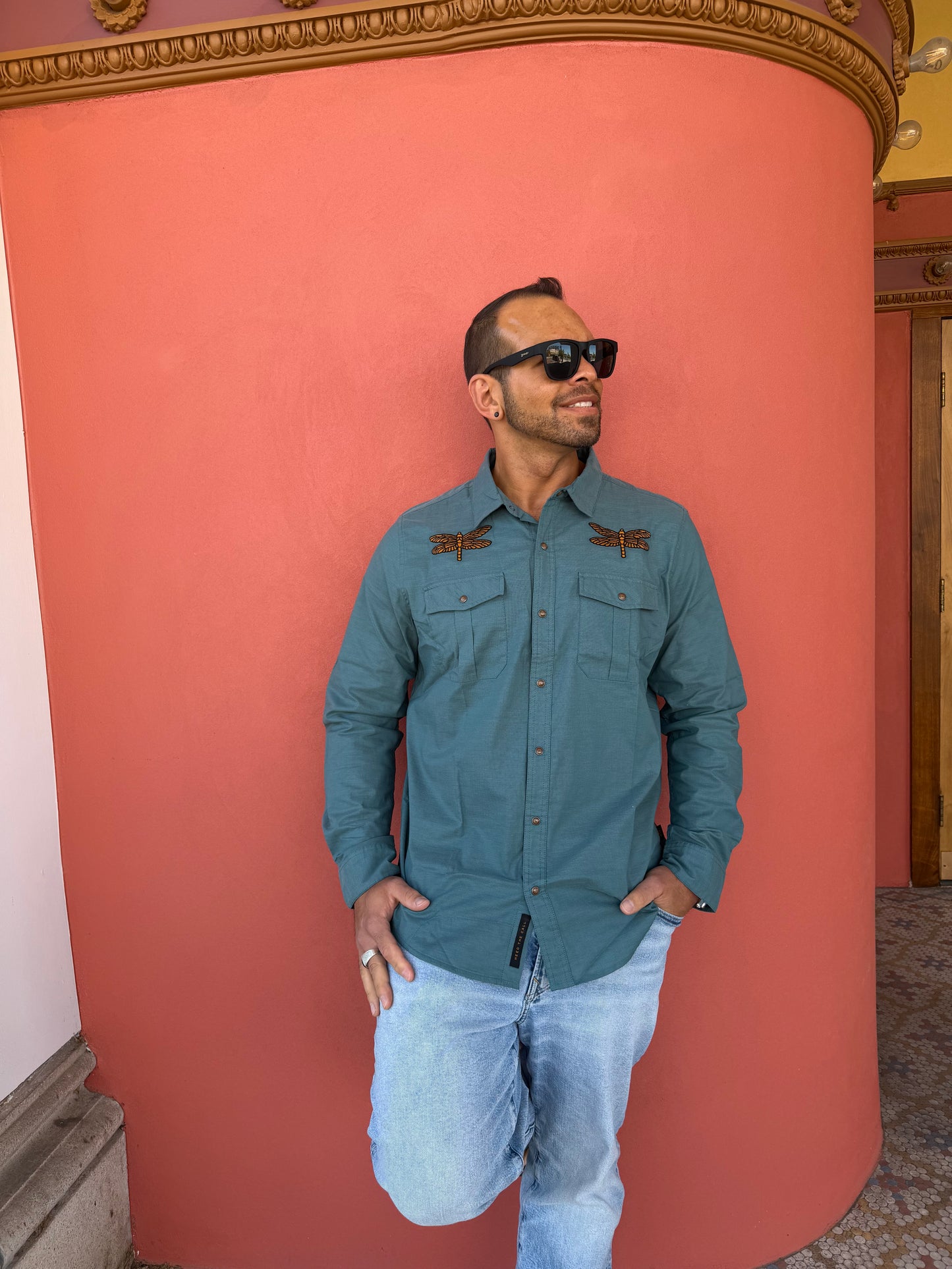 Person wearing a teal jacket and sunglasses lying on a pink couch.