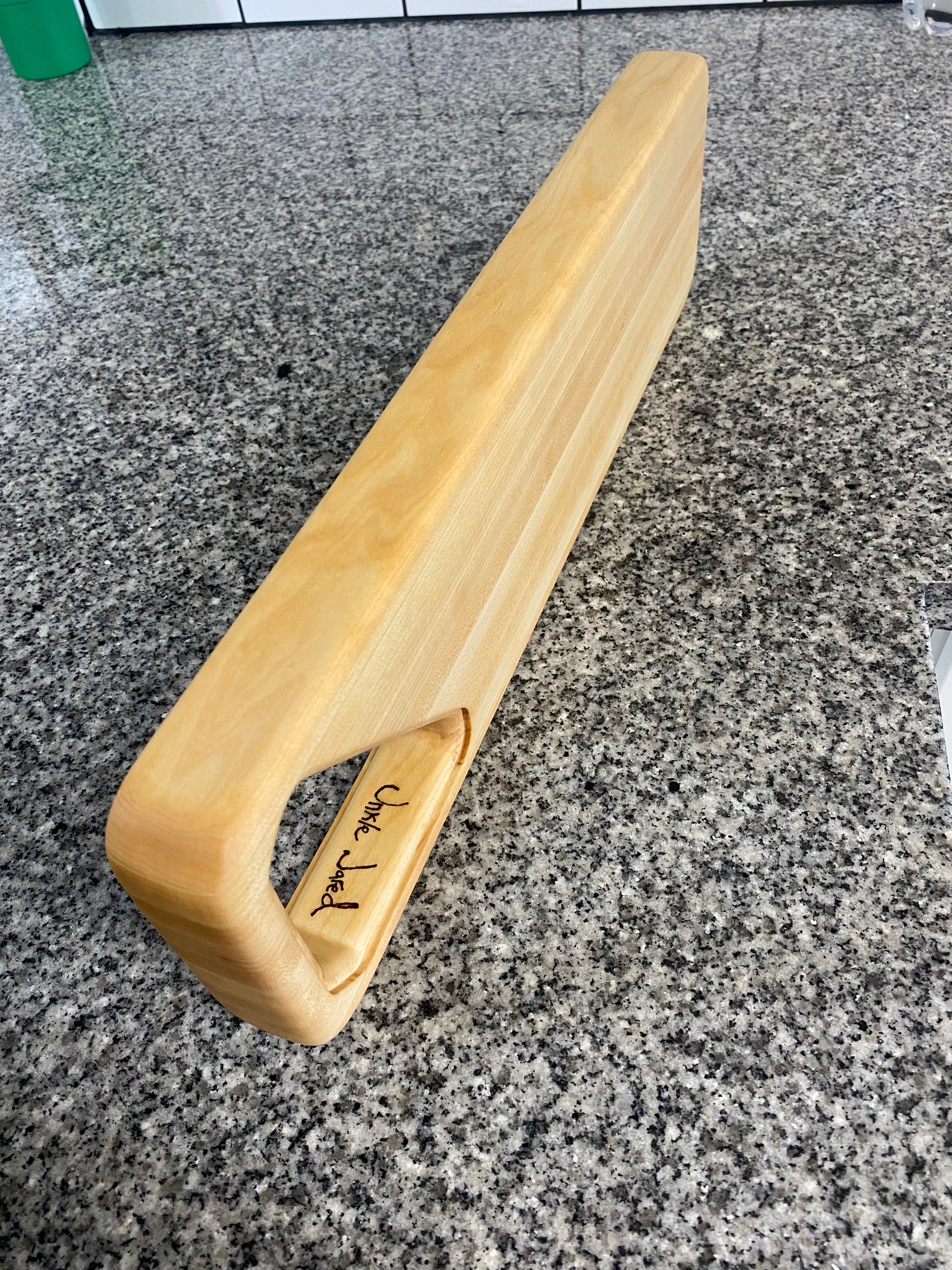 Wooden handle with 'Unkle Jared" engraving on a gray stone surface