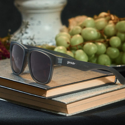 Black sunglasses with 'goodr' logo on a stack of books with grapes in the background