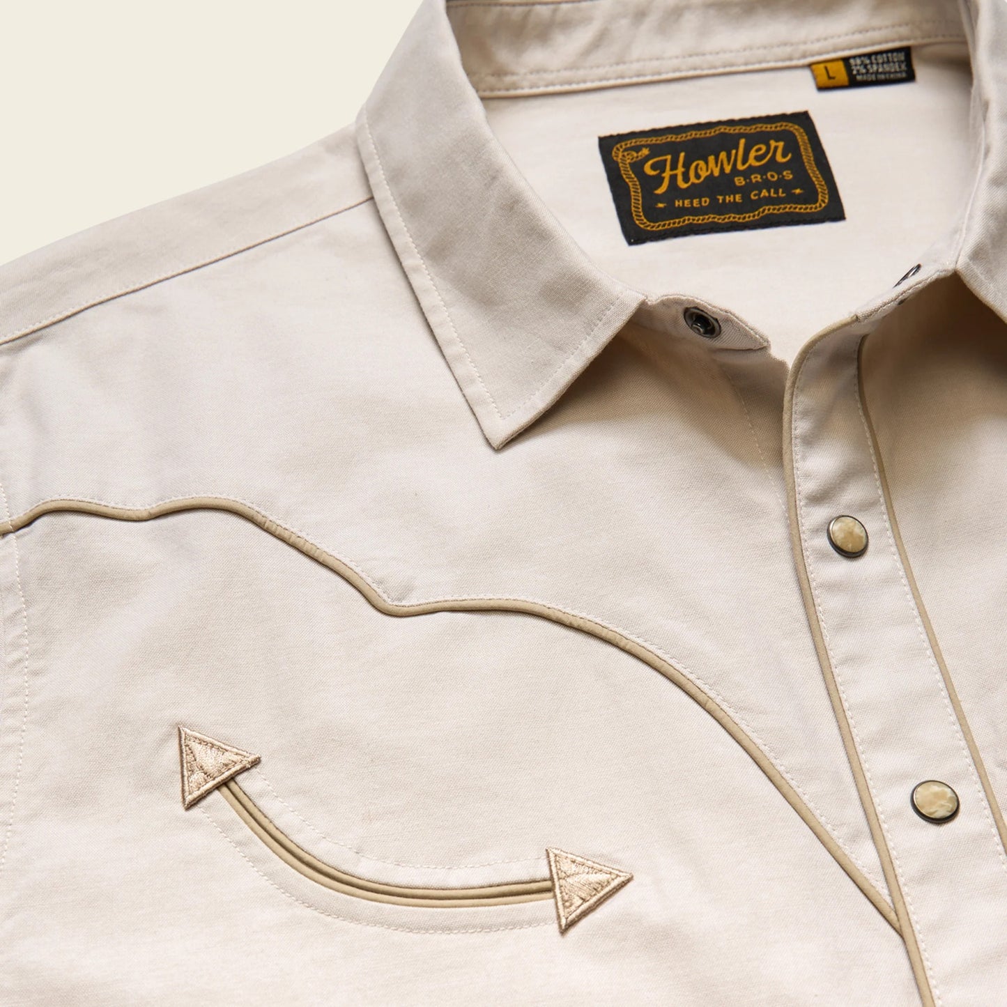 Close-up of a beige jacket with an embroidered arrow design and 'Howler Bros' label.