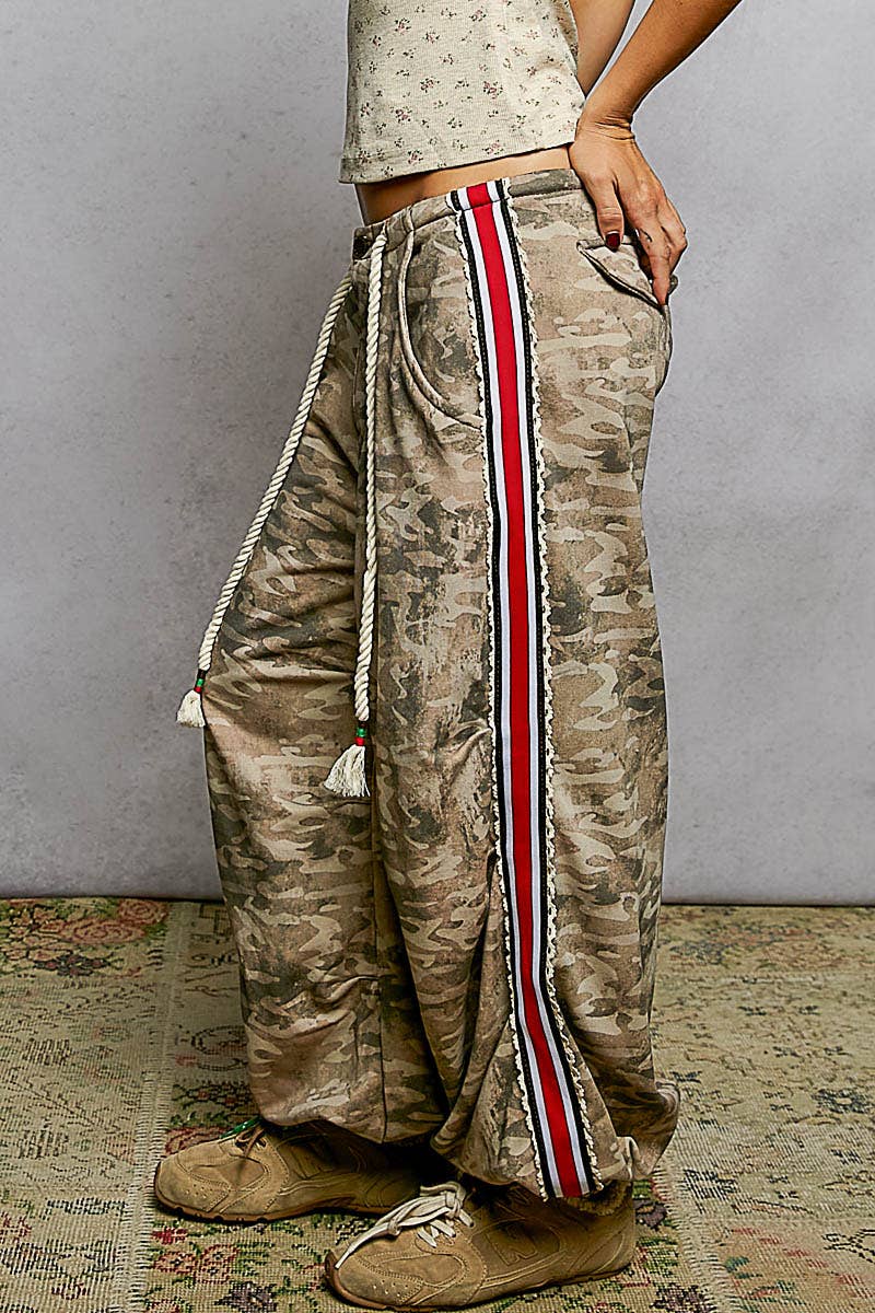 Camouflage pants with a red and white stripe worn by a person against a plain background