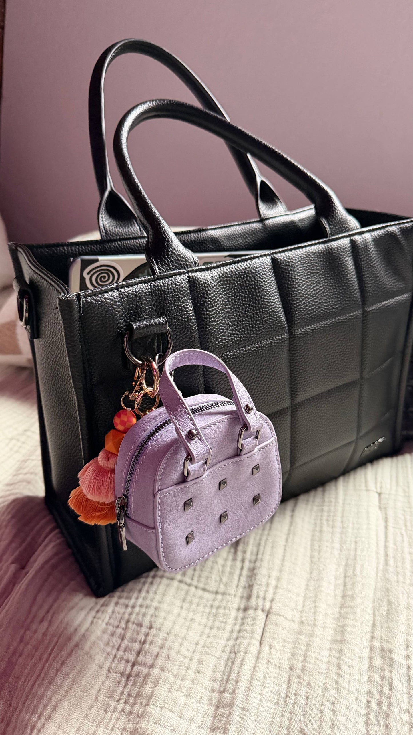 Black handbag with a small purple handbag keychain on a textured surface.