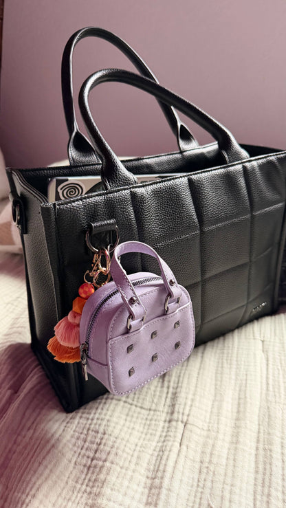Black handbag with a small purple handbag keychain on a textured surface.