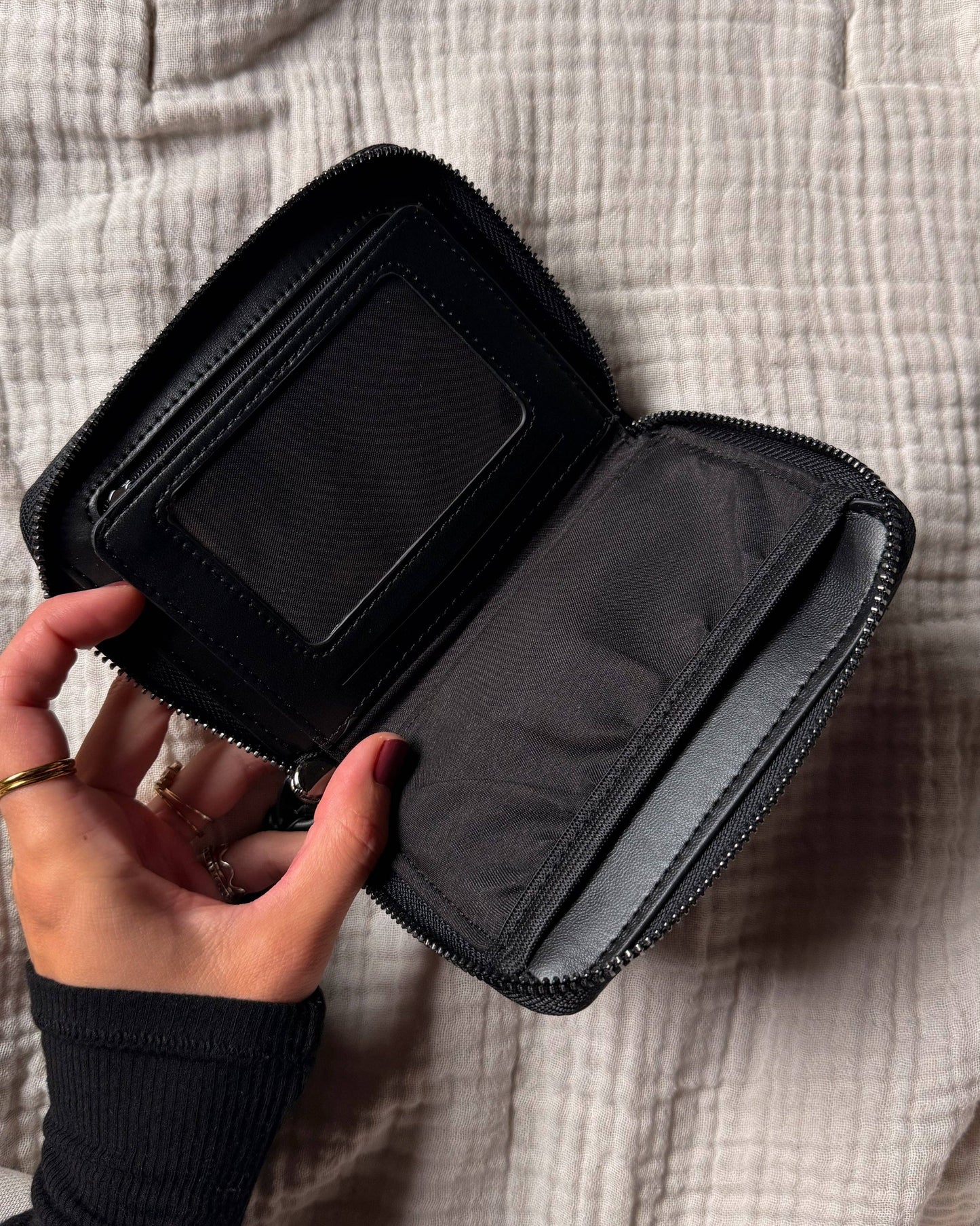 Black zippered pouch held by a hand on a textured beige surface
