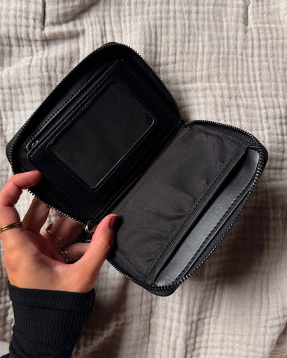 Black zippered pouch held by a hand on a textured beige surface