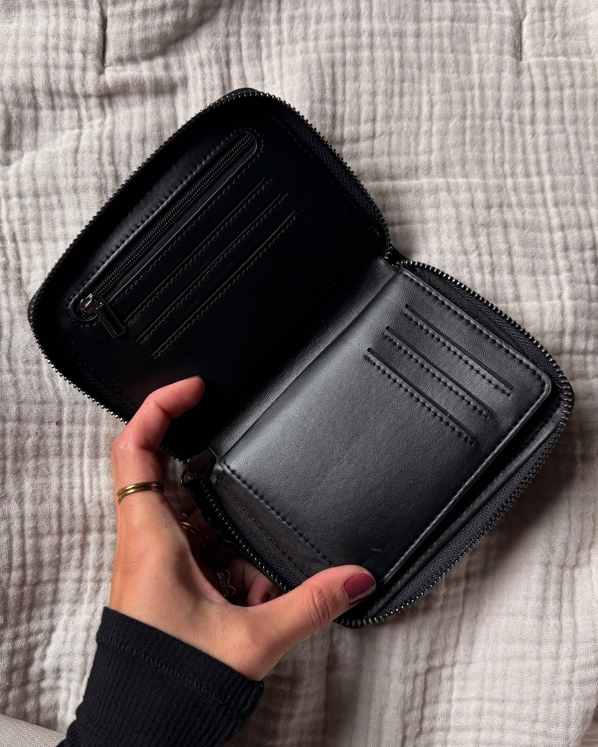 Black wallet held open by a hand on a textured surface