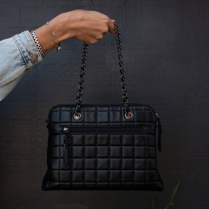 Black quilted handbag with chain handle held by a person against a dark background