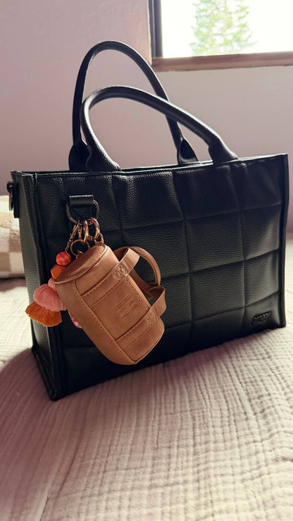 Black quilted handbag with a tan keychain on a bed
