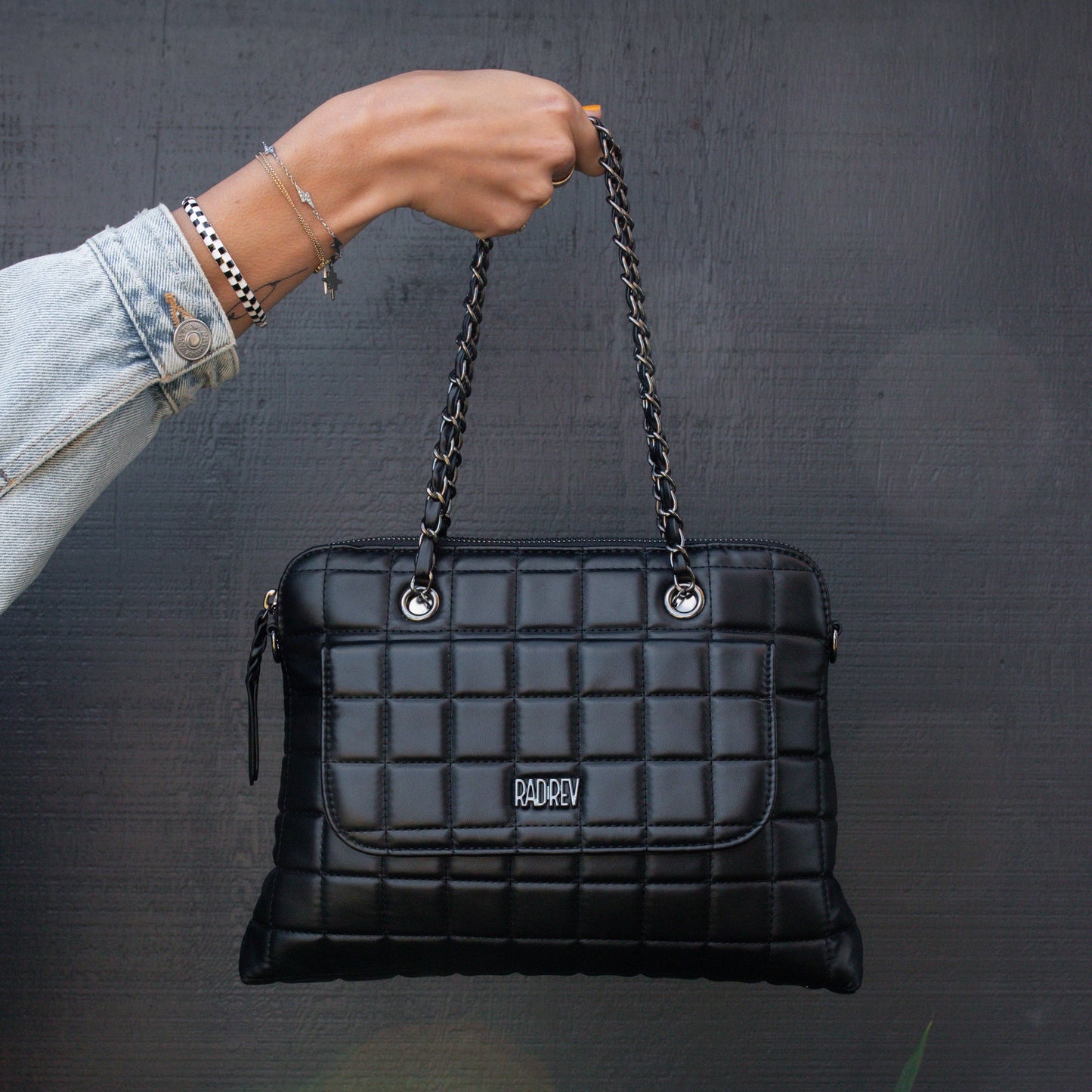 Black quilted handbag with chain handle held by a person against a dark background