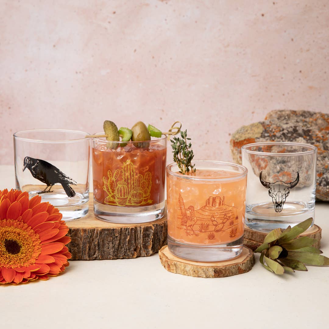 Four glasses with different designs on a wooden surface with a floral and stone background