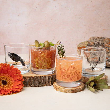Four glasses with different designs on a wooden surface with a floral and stone background
