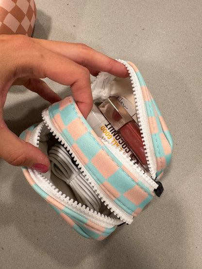 Checkered pouch with lip products and a cable held by a hand on a neutral background