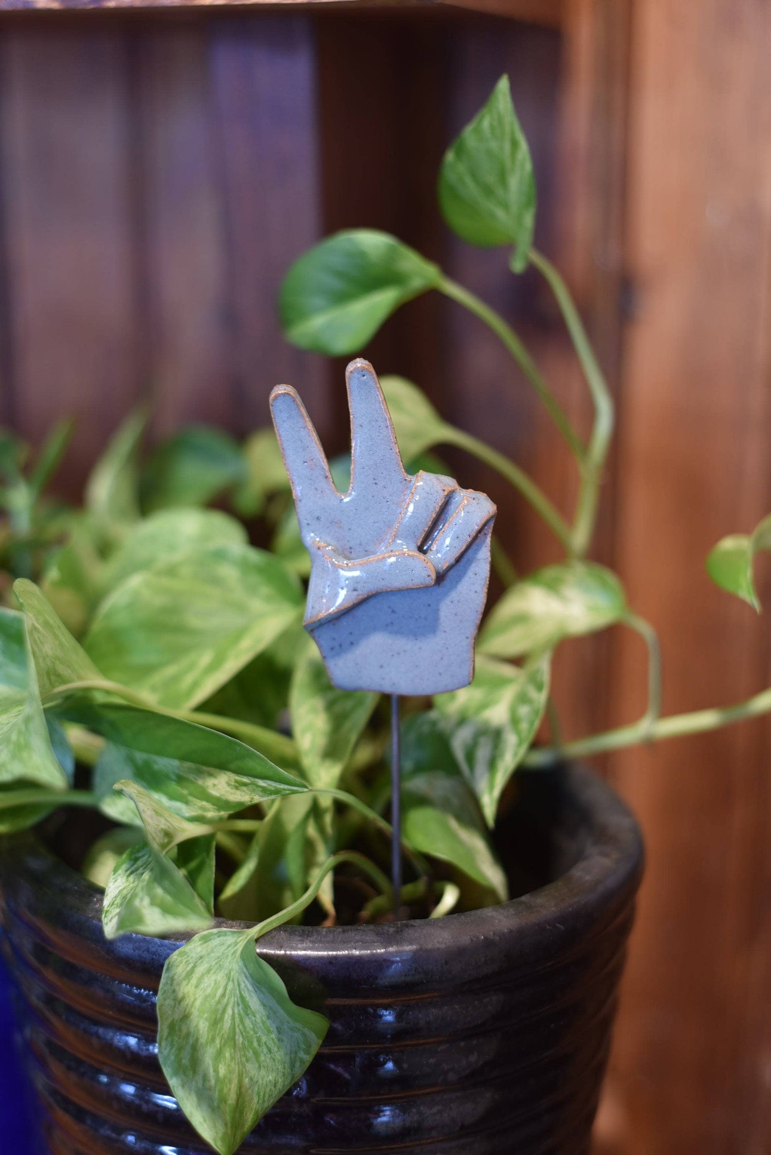 A small metal sculpture of a hand making a peace sign gesture, painted in gray color, placed in a pot with green plants.