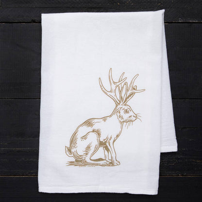 White towel with a gold rabbit with antlers design on a dark wooden surface