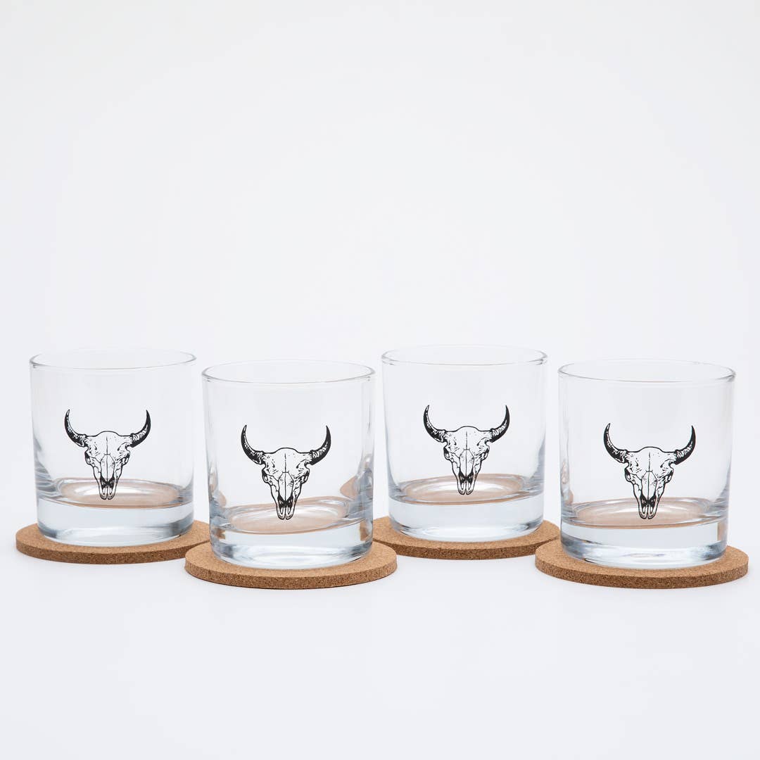 Four glass tumblers with bull skull designs on cork coasters against a white background