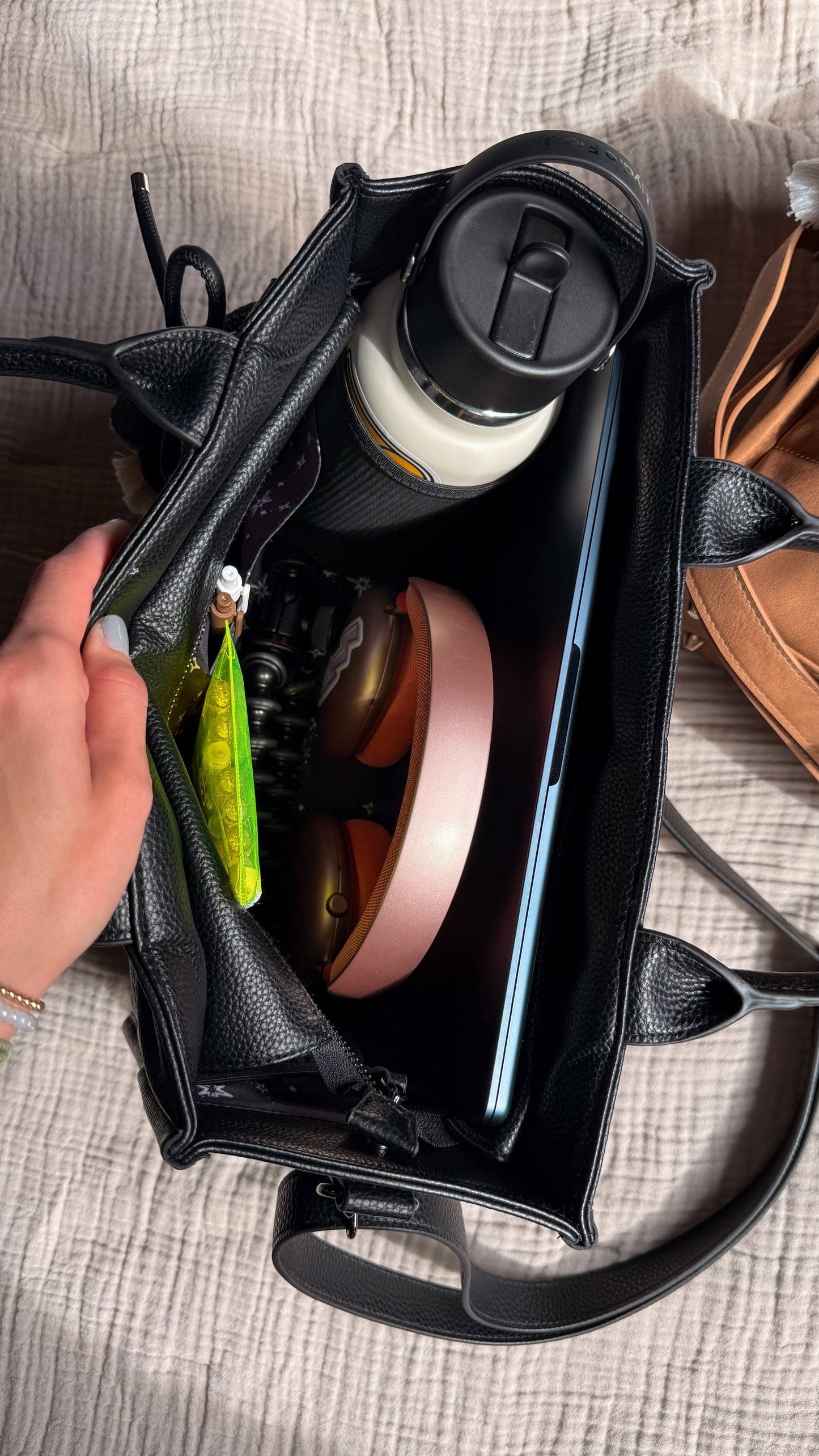 Person holding a black bag with various items including a phone, water bottle, and pink container.