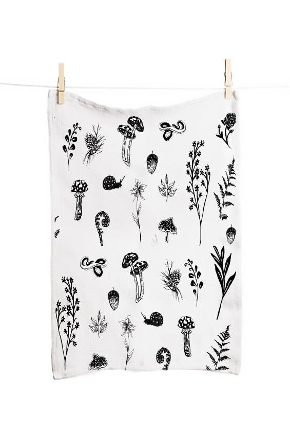 White towel with black botanical patterns hanging on a clothesline.