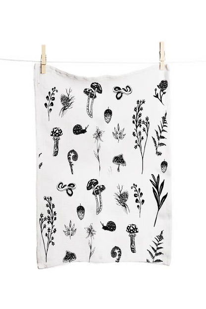 White towel with black botanical patterns hanging on a clothesline.