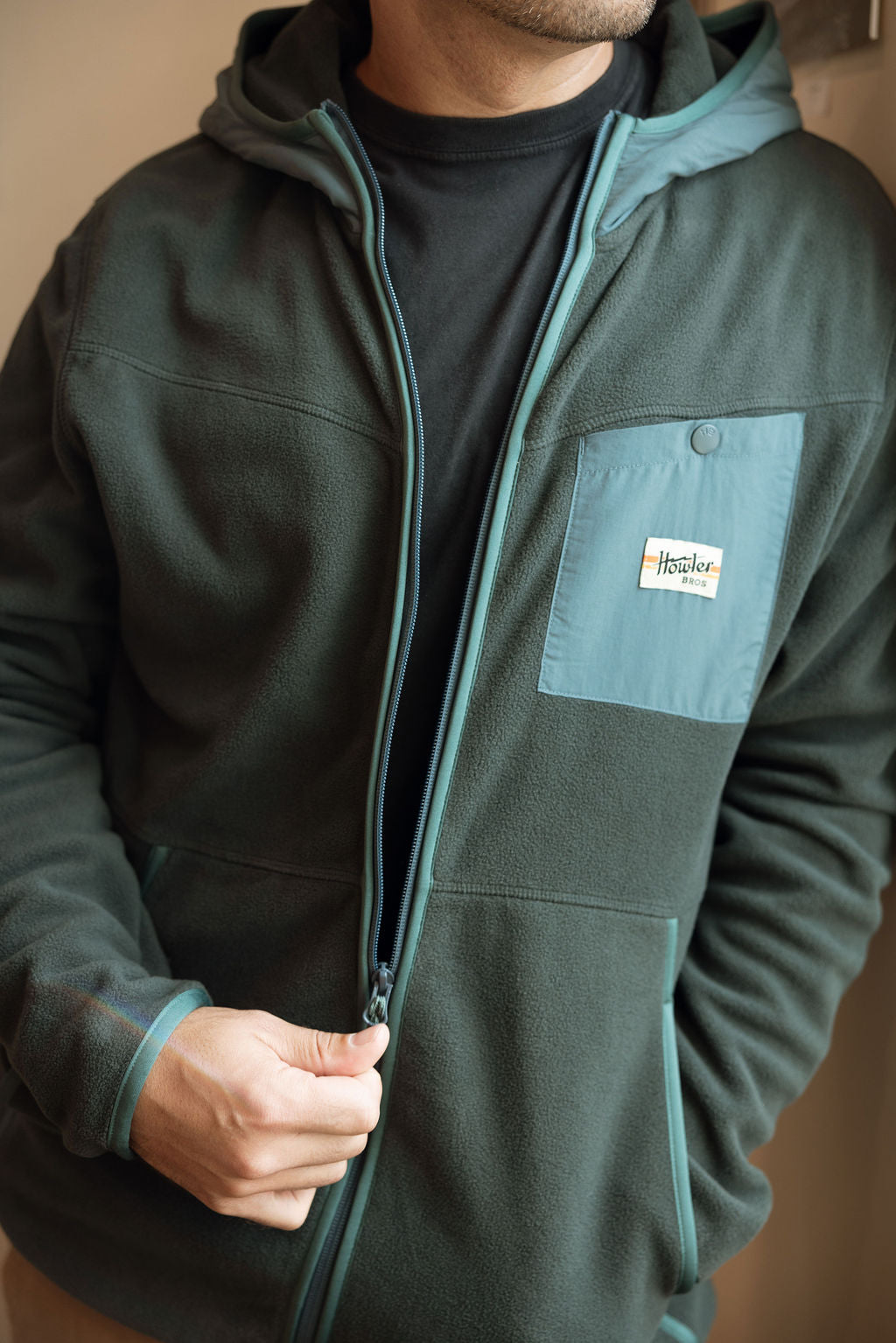 Person wearing a dark green jacket with a visible brand logo on the chest pocket.