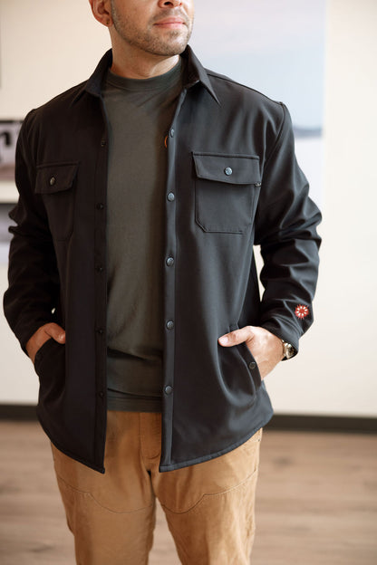 Man wearing a black jacket with a brand logo, standing indoors.