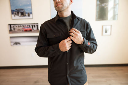 Man adjusting his black shirt in a room with framed pictures on the wall.